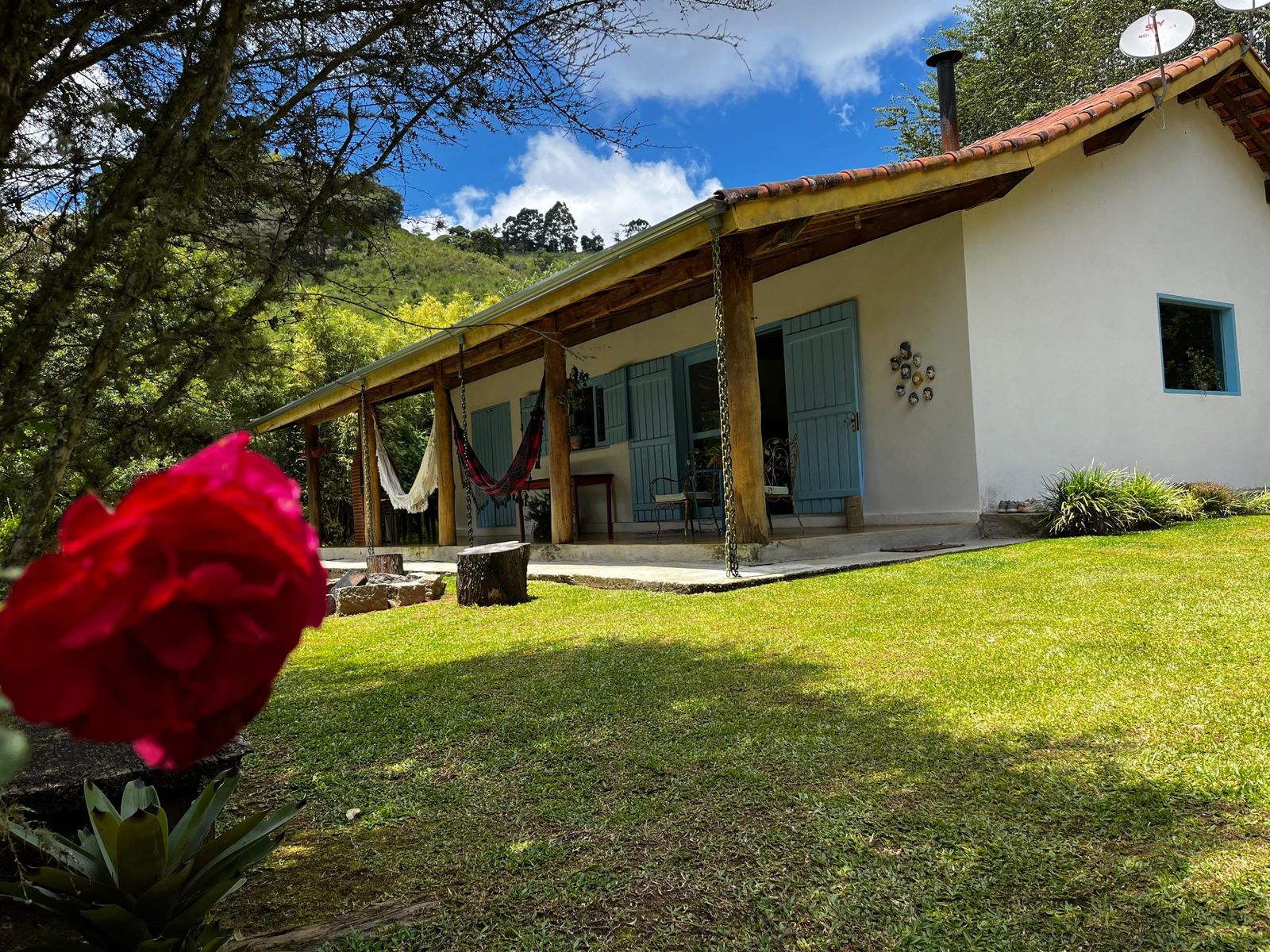 Casa Sara com varanda comprida, redes e portas azuis voltada para o jardim